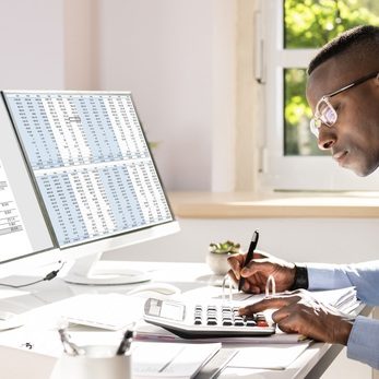 Businessperson Calculating Invoice With Computer On Desk